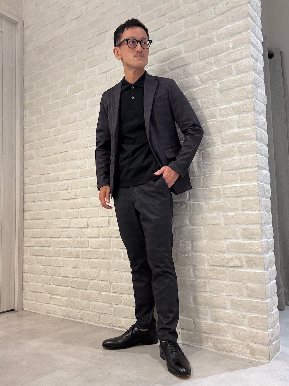グレー系のスラックス、ブラック系のポロシャツ、グレー系のテーラードジャケットを着用したメンズの秋コーディネートの2枚目の写真