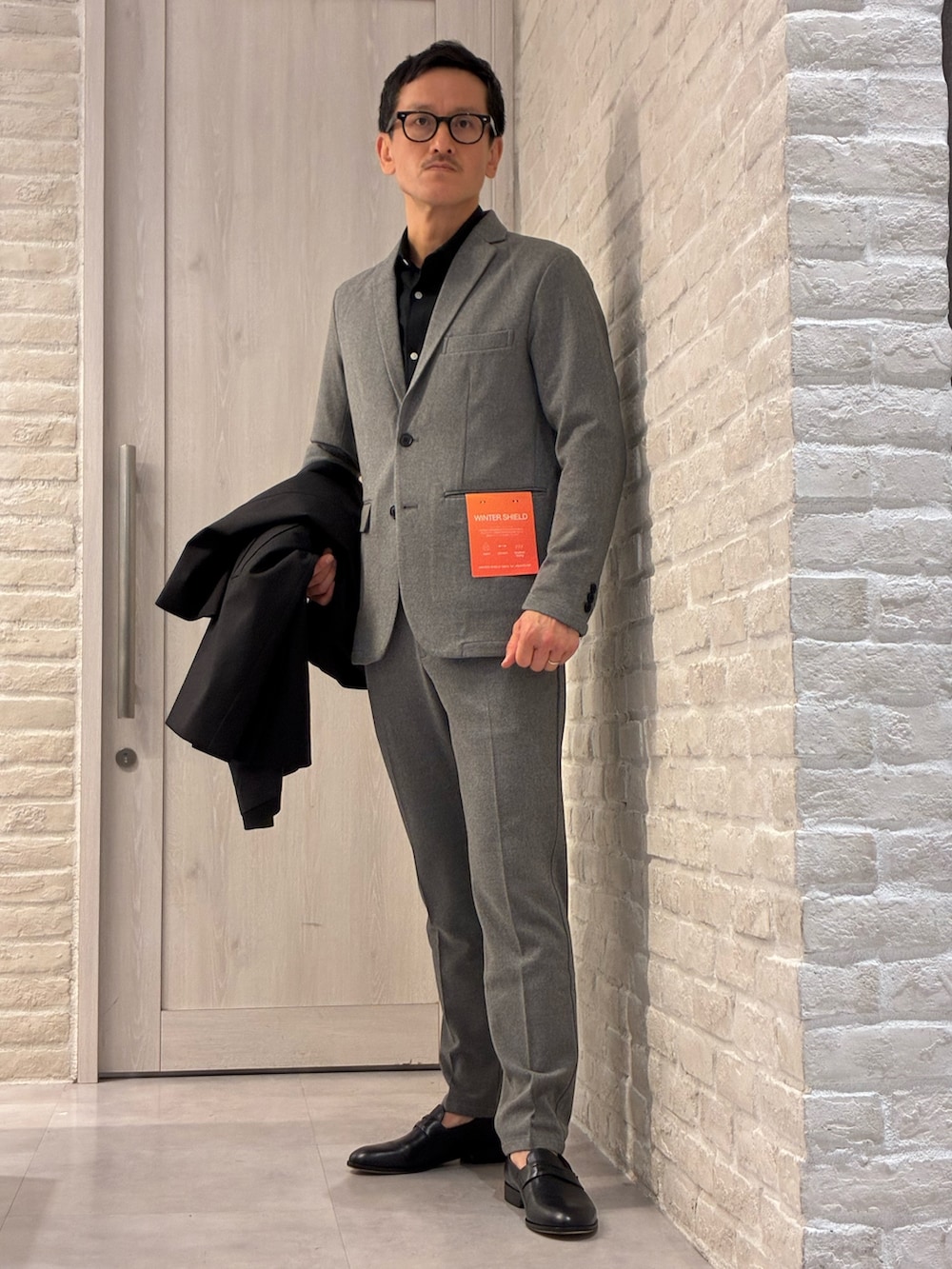 ブラック系のステンカラーコート、グレー系のセットアップ、グレー系のテーラードジャケットを着用したメンズの冬コーディネートの4枚目の写真