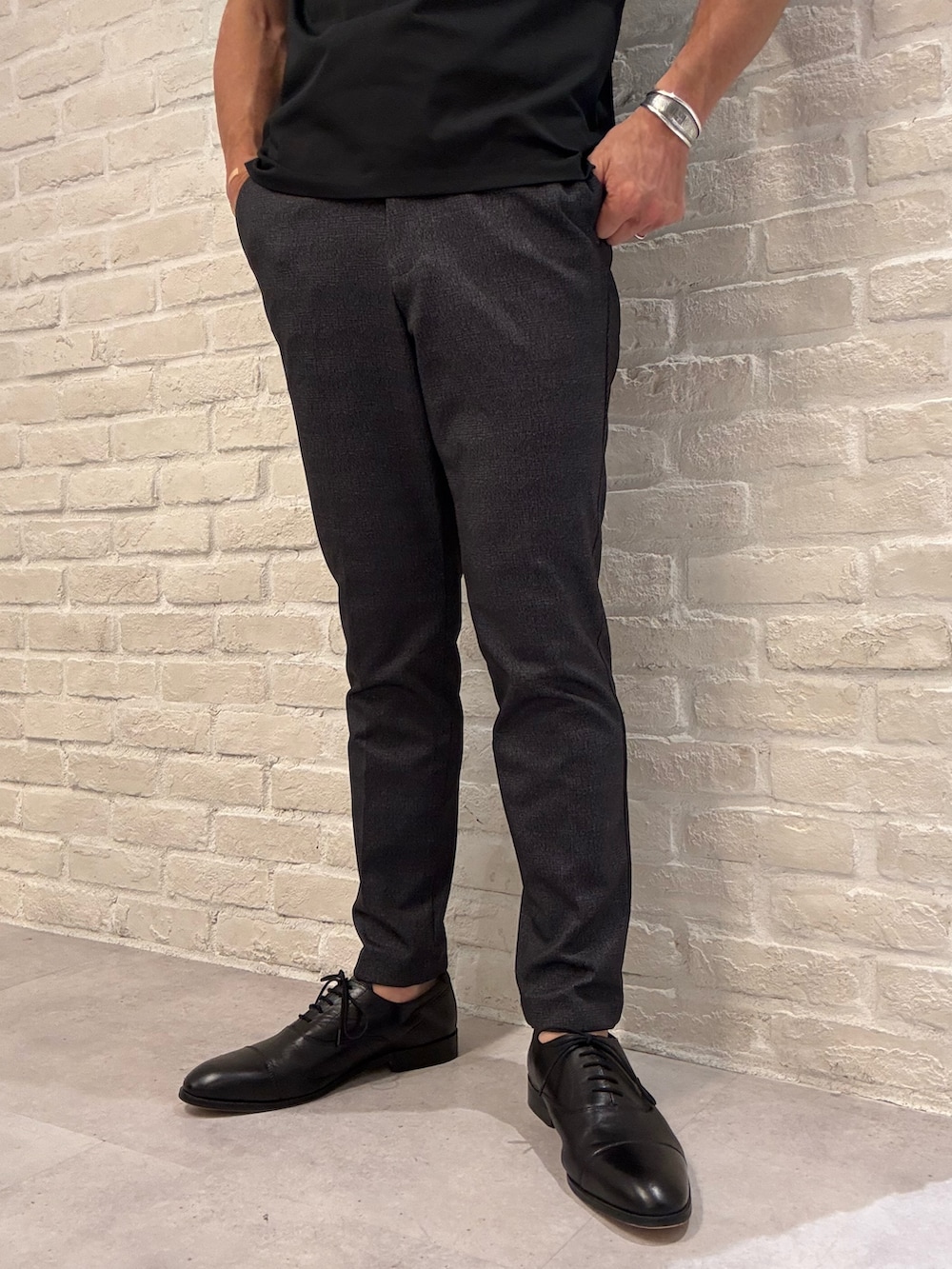 グレー系のスラックス、ブラック系のポロシャツ、グレー系のテーラードジャケットを着用したメンズの秋コーディネートの4枚目の写真