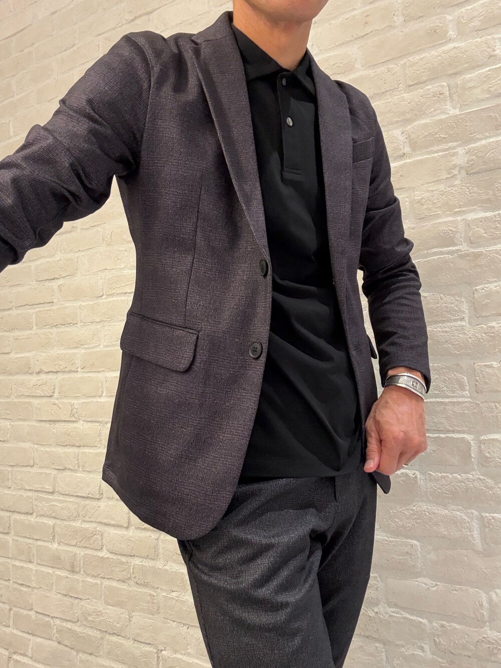 グレー系のスラックス、ブラック系のポロシャツ、グレー系のテーラードジャケットを着用したメンズの秋コーディネートの3枚目の写真