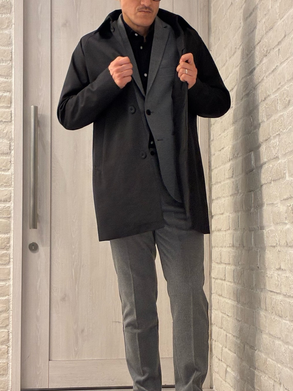 ブラック系のステンカラーコート、グレー系のセットアップ、グレー系のテーラードジャケットを着用したメンズの冬コーディネートの2枚目の写真