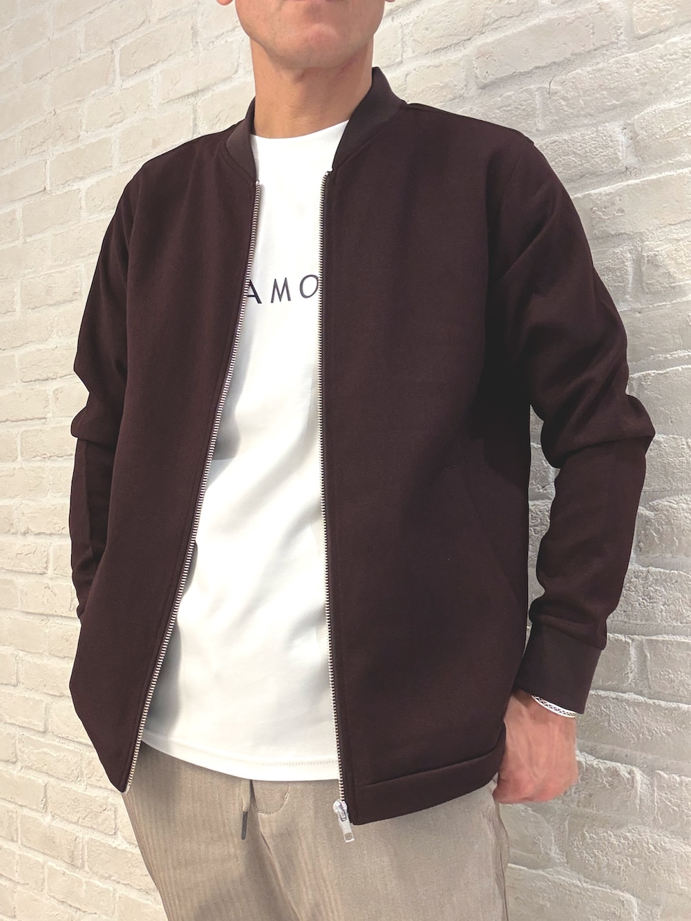 レッド系のブルゾン、ホワイト系のTシャツ/カットソー、ベージュ系のスラックスを着用したメンズの秋コーディネートの3枚目の写真