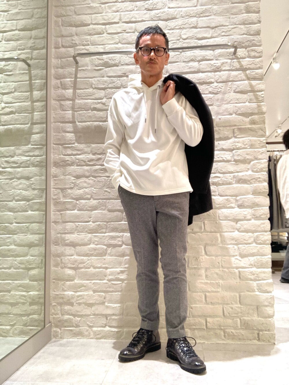 ブラック系のチェスターコート、ホワイト系のパーカー、グレー系のスラックスを着用したメンズの秋コーディネートの4枚目の写真