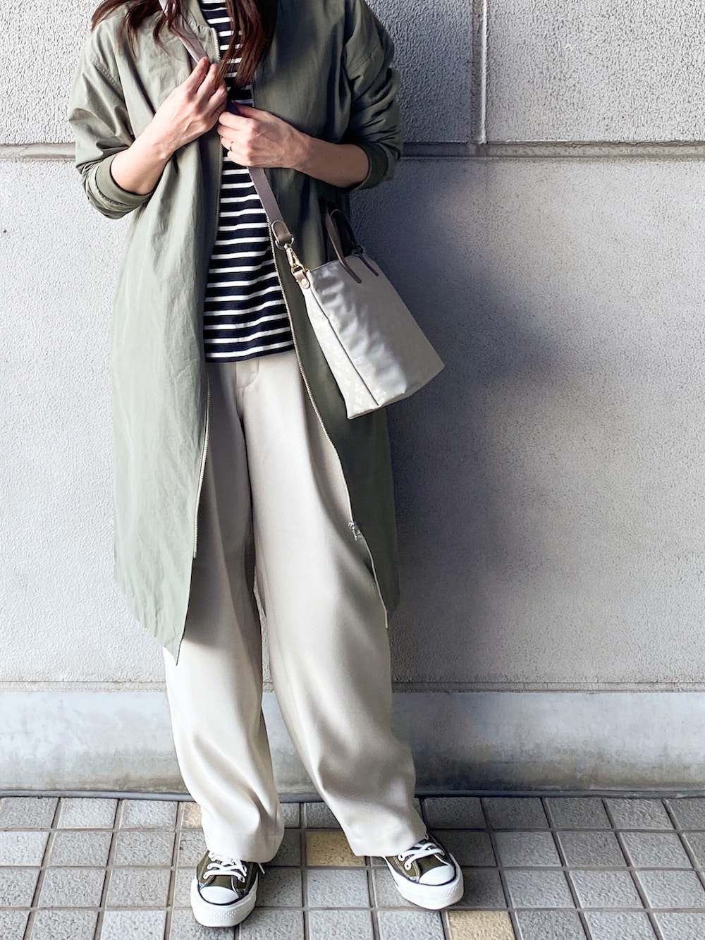 グリーン系のノーカラーコート、ブラック系のTシャツ/カットソー、ホワイト系のスラックスを着用したレディースの春コーディネートの3枚目の写真