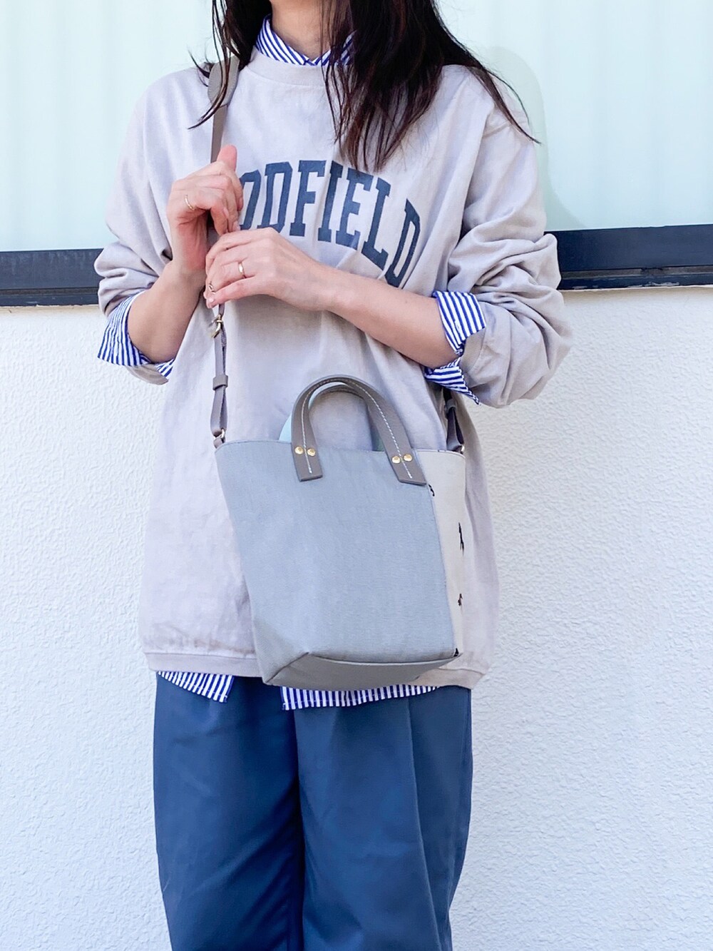グレー系のショルダーバッグ、ブルー系のスラックス、ホワイト系のスニーカーを着用したレディースの春コーディネートの2枚目の写真
