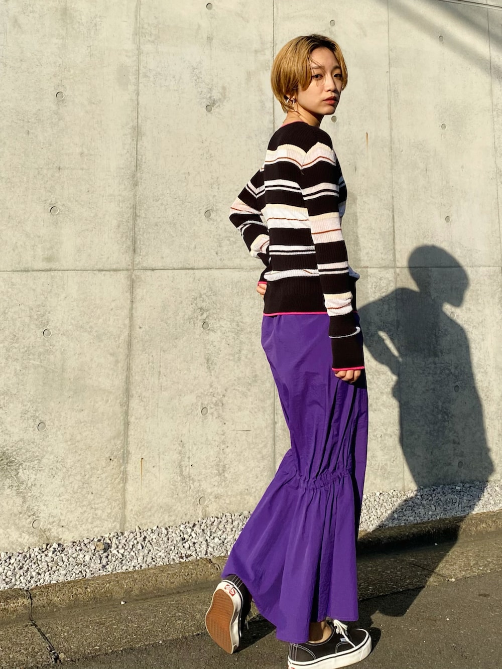 パープル系のスカート、ブラック系のニット/セーター、ブラック系のスニーカーを着用したレディースの冬コーディネートの2枚目の写真