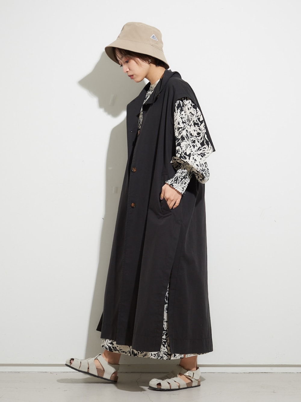 ホワイト系のサンダル、ホワイト系のワンピース、ブラック系のトレンチコートを着用したレディースの冬コーディネートの2枚目の写真