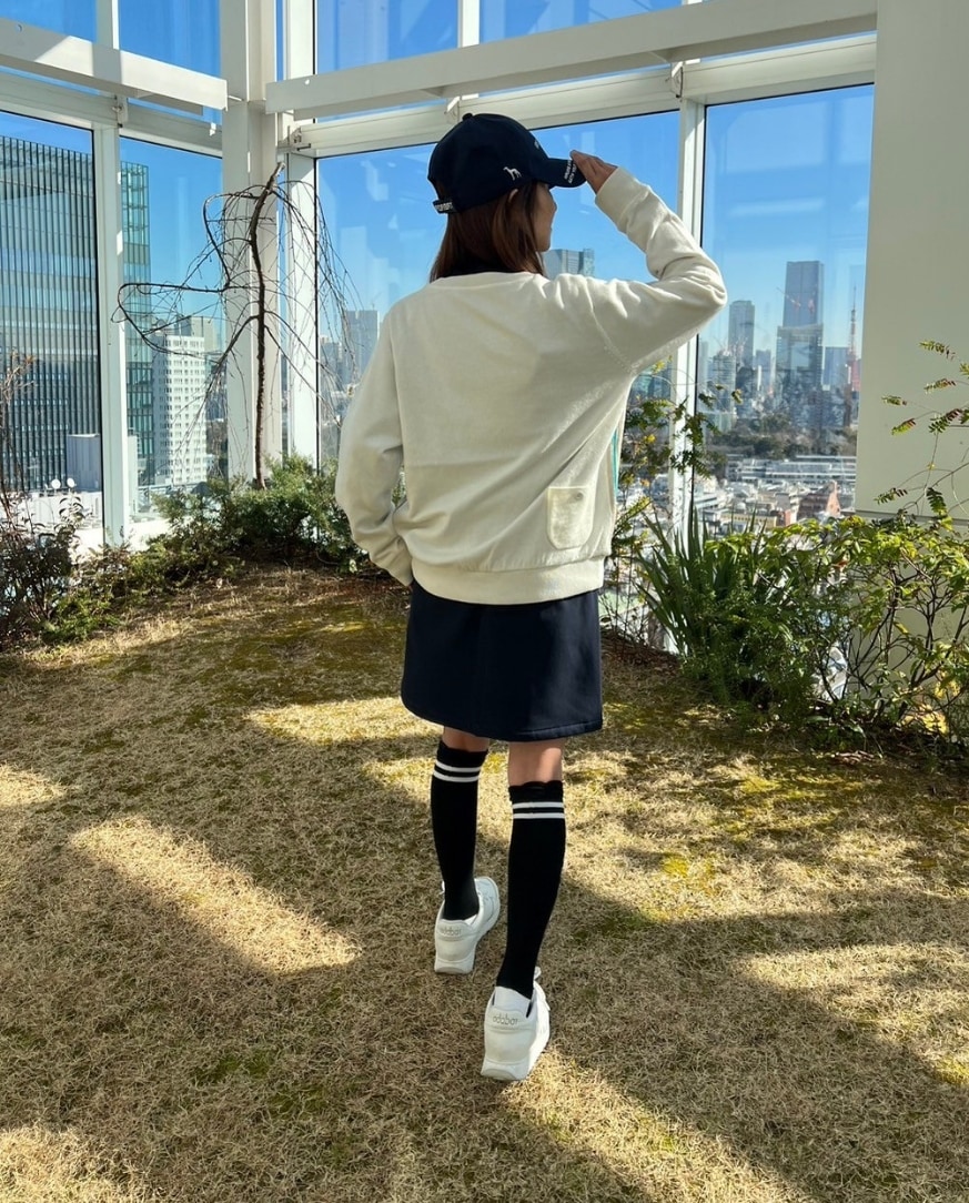 ホワイト系のニット/セーター、ブルー系のスカート、ブルー系のゴルフグッズを着用したレディースの冬コーディネートの2枚目の写真