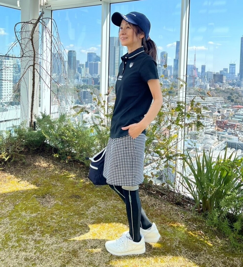 ブラック系のポロシャツ、ブルー系のハンドバッグ、ブルー系のスカートを着用したレディースの春コーディネートの2枚目の写真