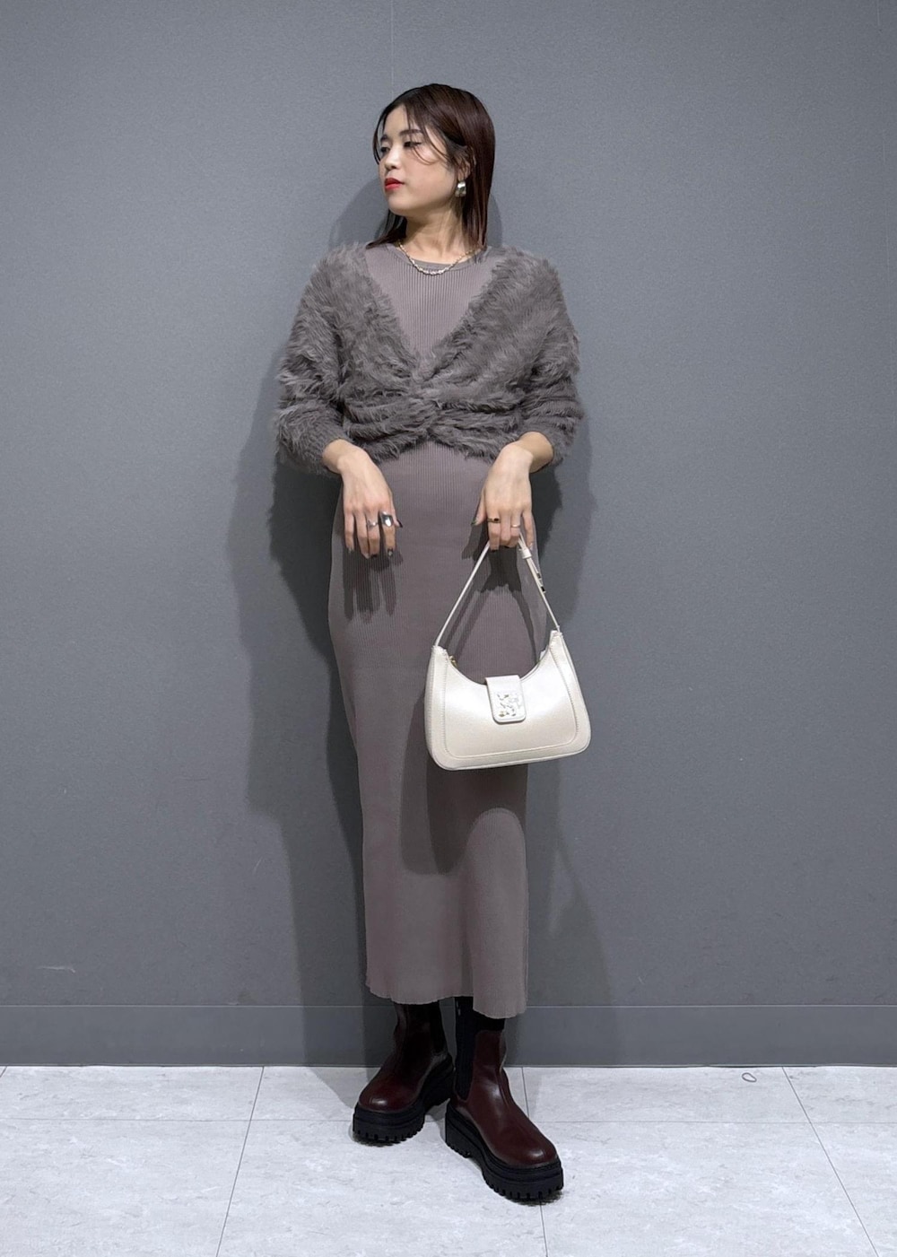 ホワイト系のハンドバッグ、ブラウン系のブーツ、ベージュ系のワンピースを着用したレディースの冬コーディネートの2枚目の写真