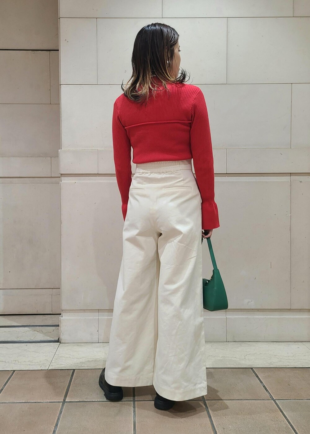 グリーン系のハンドバッグ、ホワイト系のスラックス、レッド系のニット/セーターを着用したレディースの冬コーディネートの3枚目の写真