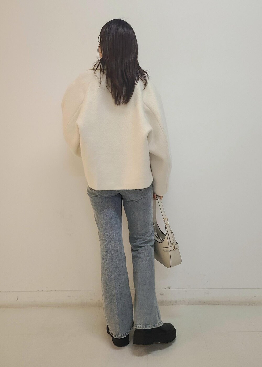 ブルー系のデニムパンツ、ブラック系のブーツ、ホワイト系のハンドバッグを着用したレディースの秋コーディネートの5枚目の写真