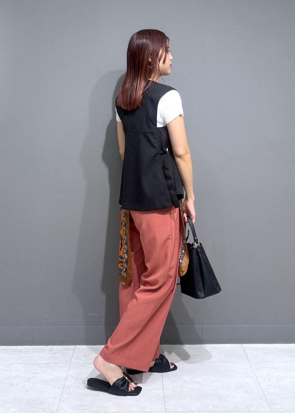 ブラック系のサンダル、ホワイト系のニット/セーター、オレンジ系のスラックスを着用したレディースの夏コーディネートの3枚目の写真