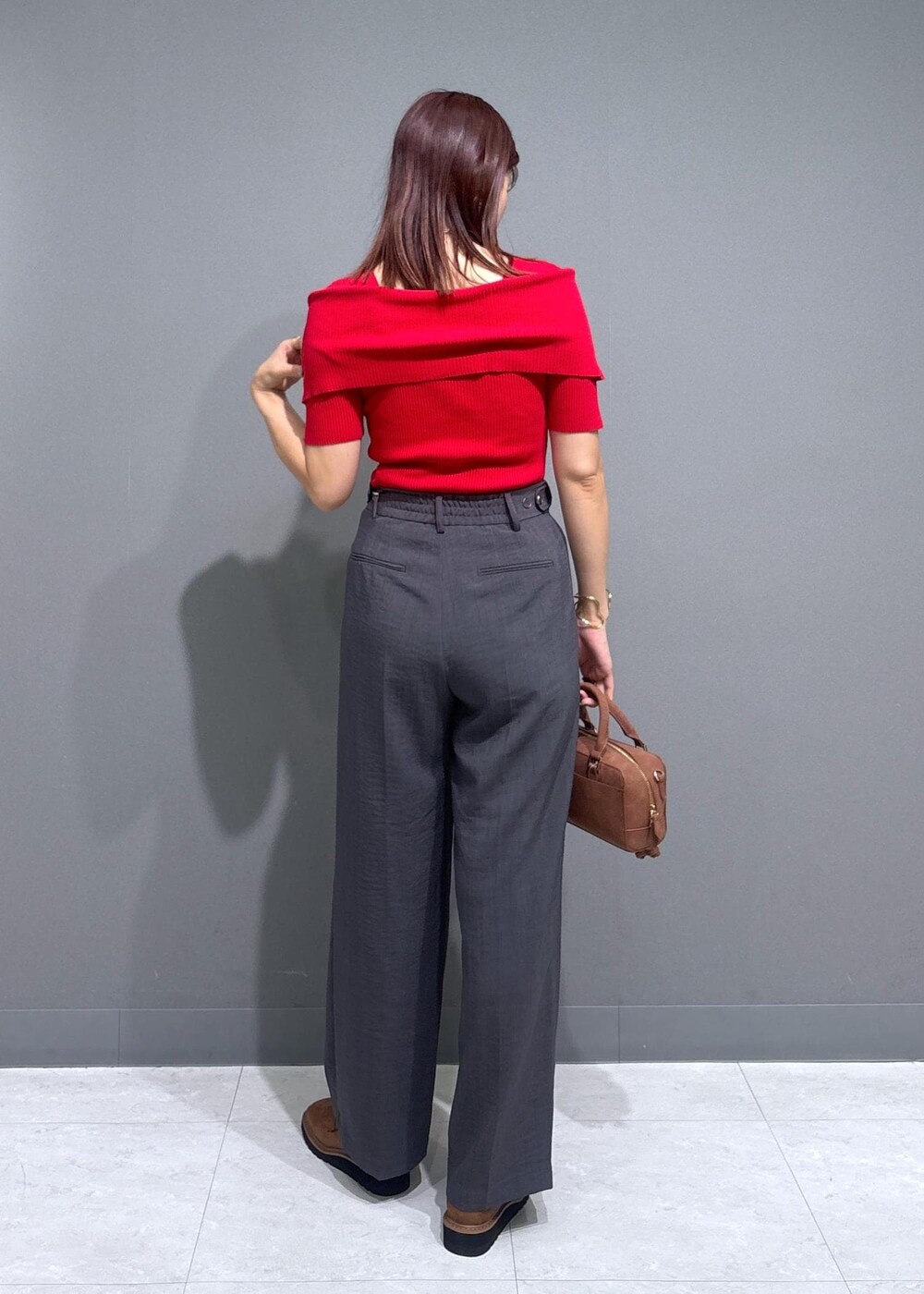 グレー系のスラックス、ブラウン系のボストンバッグ、レッド系のニット/セーターを着用したレディースの夏コーディネートの3枚目の写真