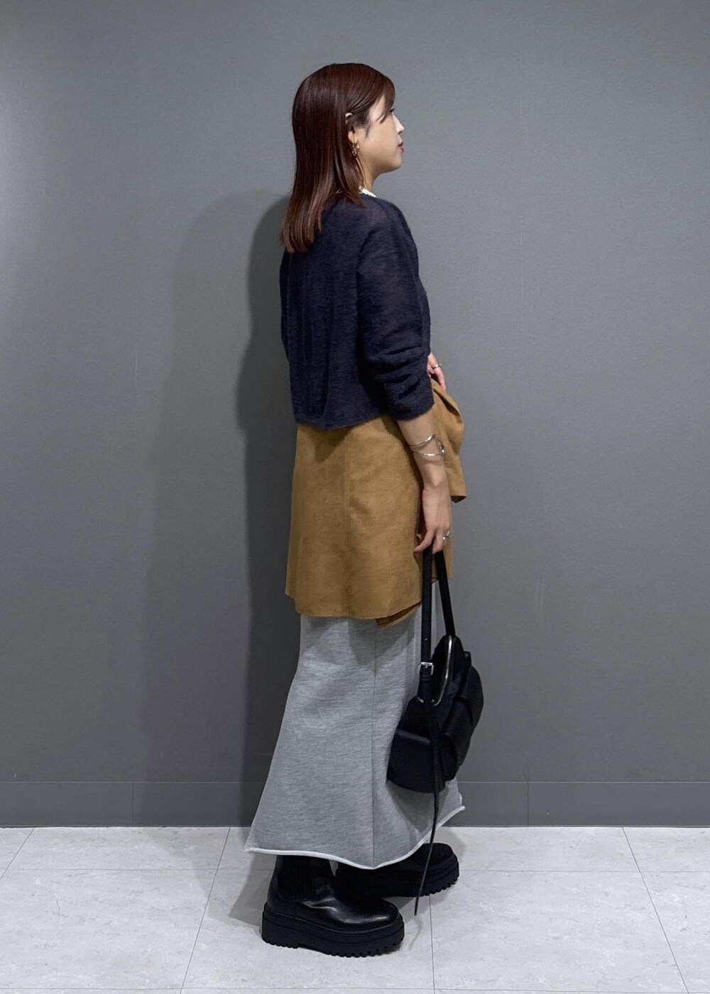 グレー系のニット/セーター、グレー系のスカート、ブラック系のショルダーバッグを着用したレディースの秋コーディネートの2枚目の写真