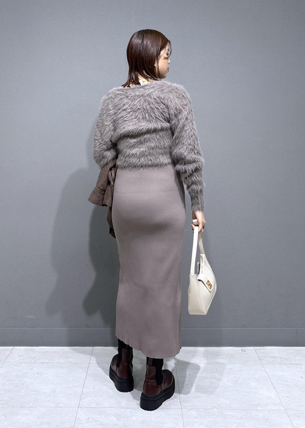 ホワイト系のハンドバッグ、ブラウン系のブーツ、ベージュ系のワンピースを着用したレディースの冬コーディネートの4枚目の写真