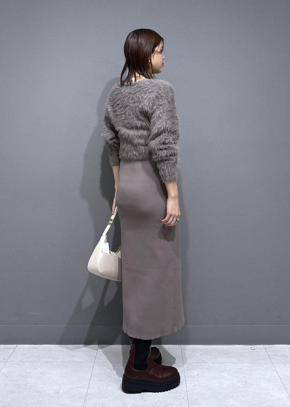 ホワイト系のハンドバッグ、ブラウン系のブーツ、ベージュ系のワンピースを着用したレディースの冬コーディネートの3枚目の写真