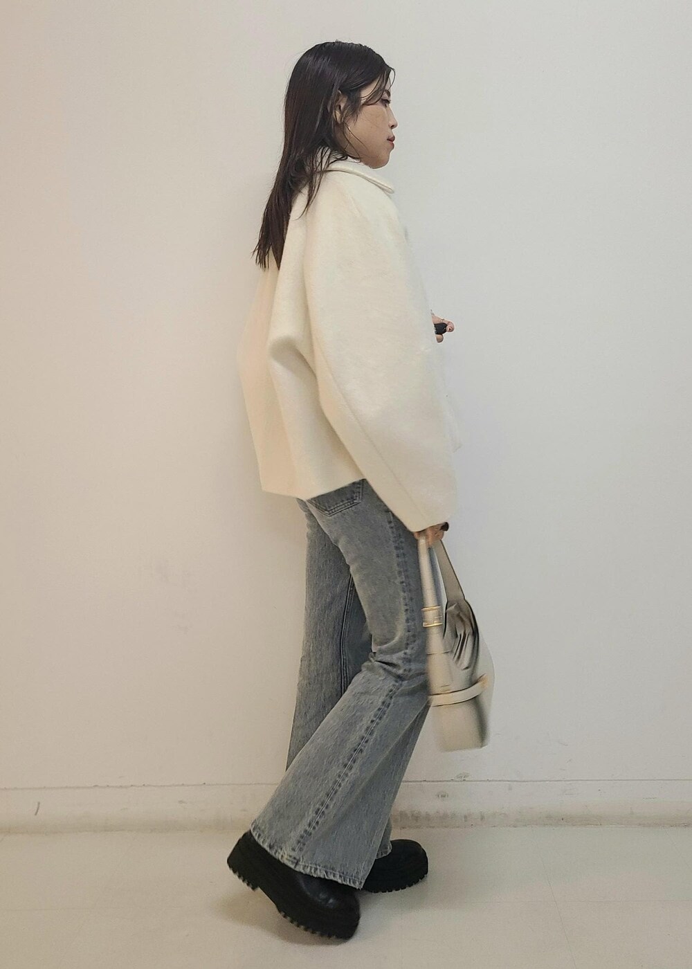 ブルー系のデニムパンツ、ブラック系のブーツ、ホワイト系のハンドバッグを着用したレディースの秋コーディネートの3枚目の写真