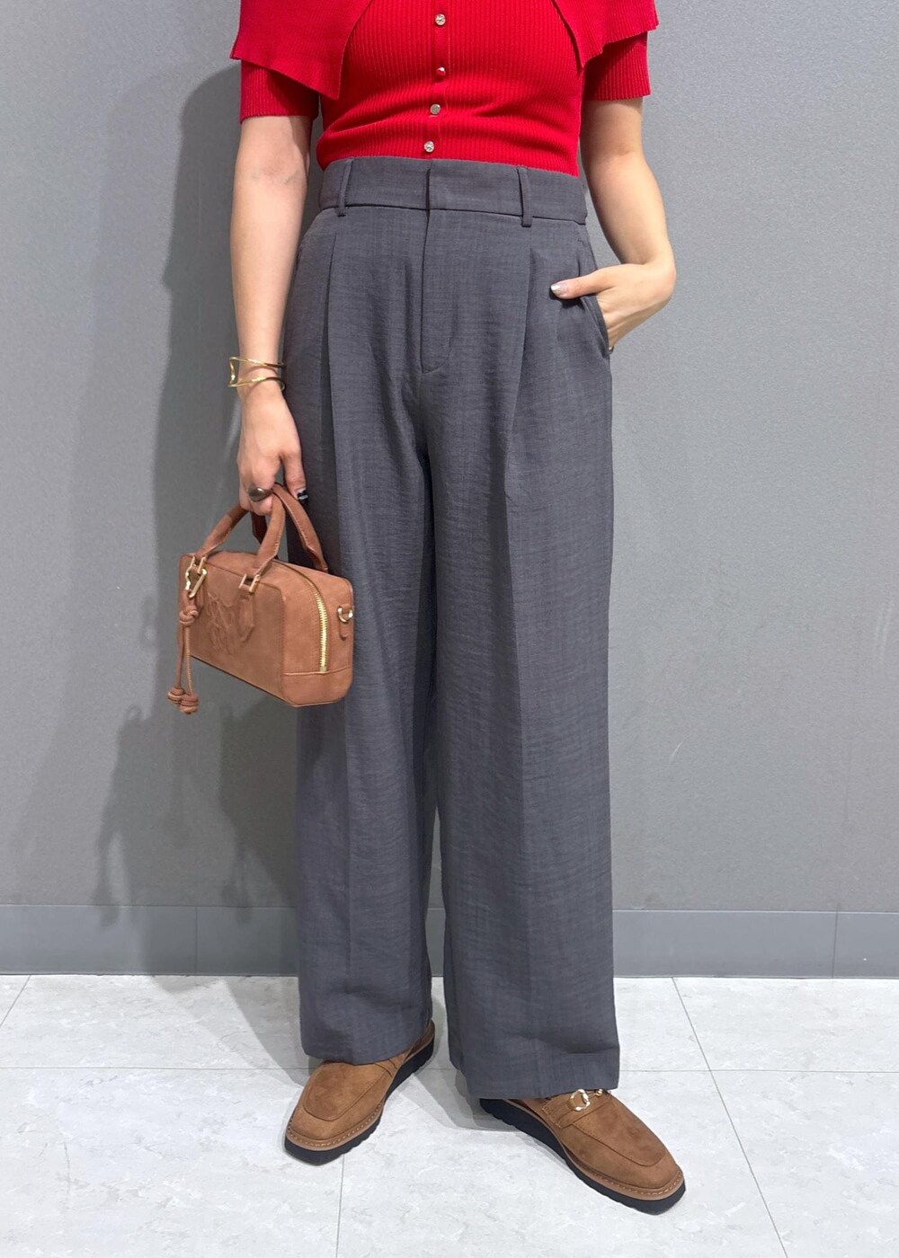 グレー系のスラックス、ブラウン系のボストンバッグ、レッド系のニット/セーターを着用したレディースの夏コーディネートの6枚目の写真