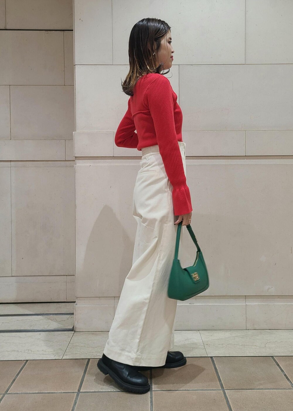 グリーン系のハンドバッグ、ホワイト系のスラックス、レッド系のニット/セーターを着用したレディースの冬コーディネートの2枚目の写真