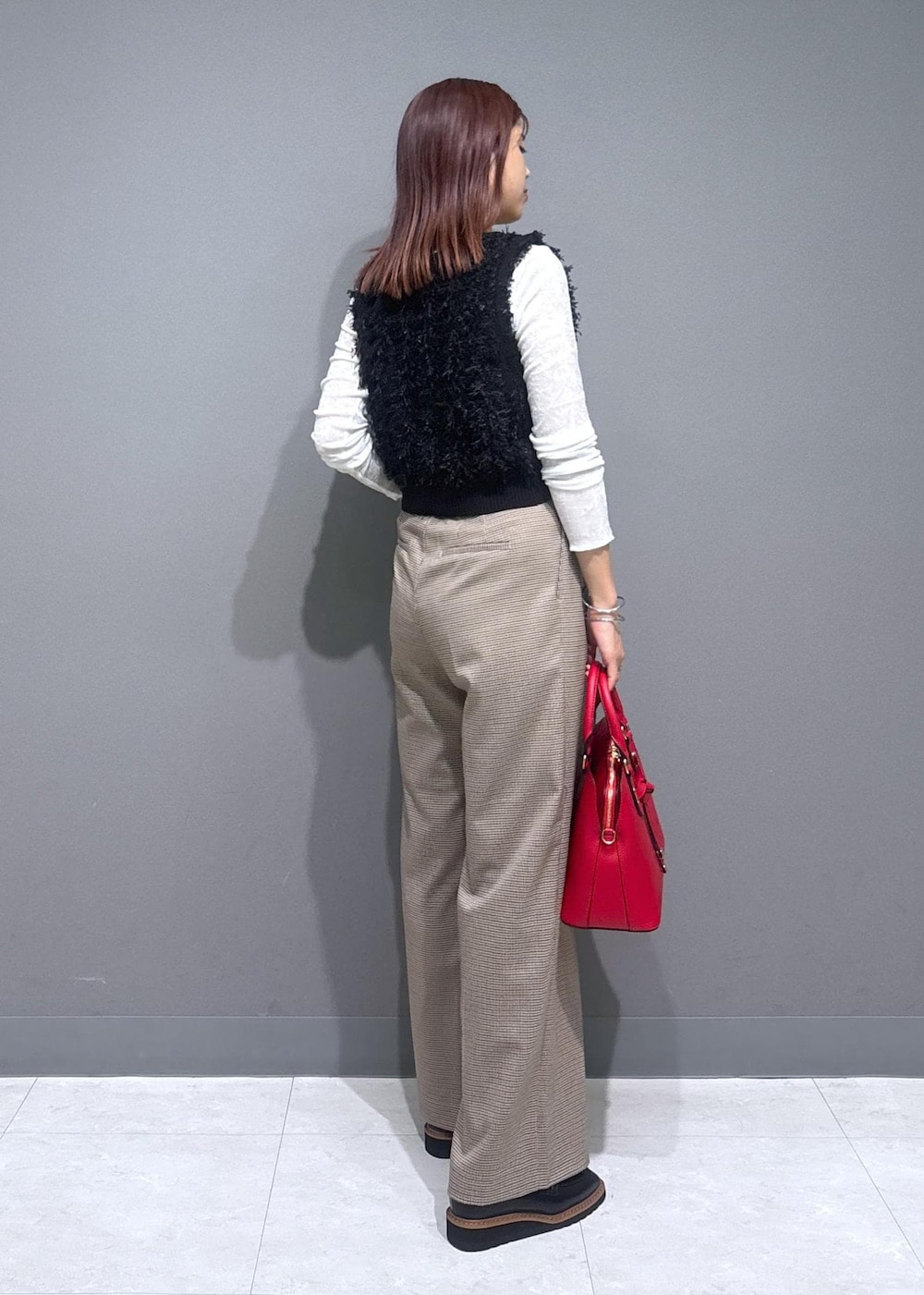 ベージュ系のスラックス、レッド系のボストンバッグ、ブラック系のベストを着用したレディースの秋コーディネートの3枚目の写真