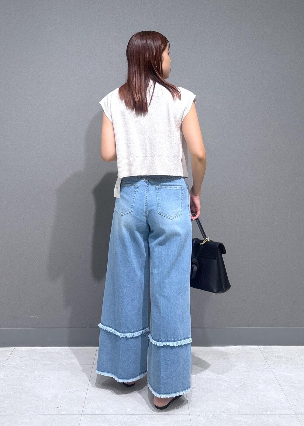 ブラック系のハンドバッグ、ブラック系のサンダル、ブルー系のデニムパンツを着用したレディースの夏コーディネートの2枚目の写真