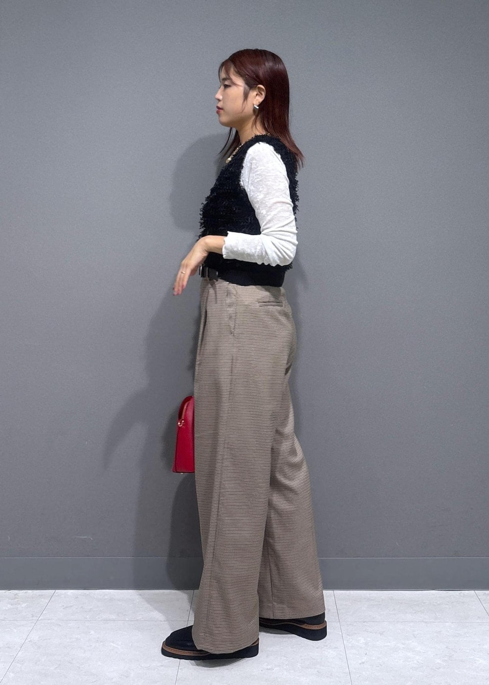 ベージュ系のスラックス、レッド系のボストンバッグ、ブラック系のベストを着用したレディースの秋コーディネートの2枚目の写真