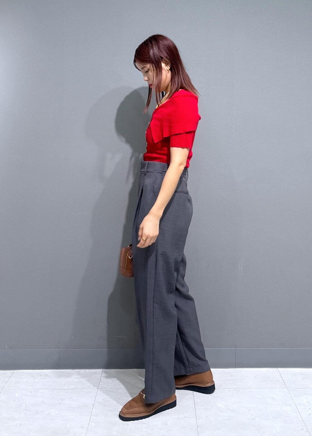 グレー系のスラックス、ブラウン系のボストンバッグ、レッド系のニット/セーターを着用したレディースの夏コーディネートの2枚目の写真