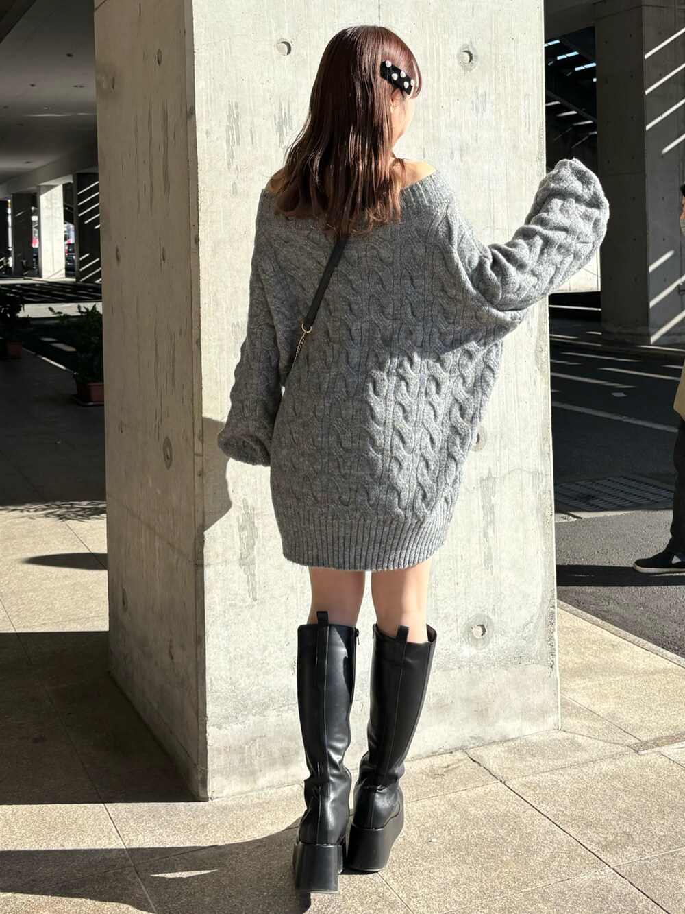 グレー系のワンピース、ブラック系のショルダーバッグ、ブラック系のブーツを着用したレディースの秋コーディネートの2枚目の写真