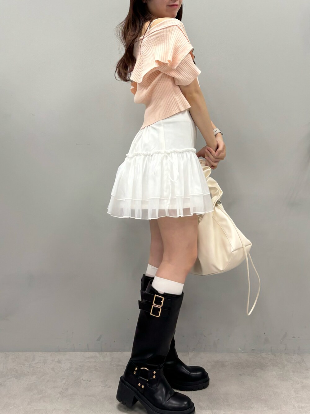 ピンク系のニット/セーター、ホワイト系のスカート、ブラック系のブーツを着用したレディースの春コーディネートの2枚目の写真