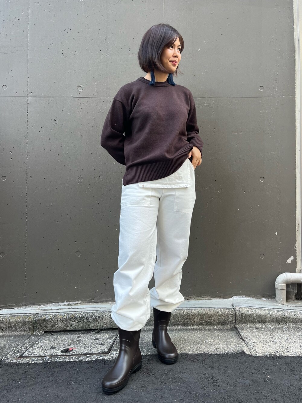 ブラウン系のニット/セーター、ホワイト系のサロペット/オーバーオール、ブラウン系のレインシューズを着用したレディースの秋コーディネートの3枚目の写真