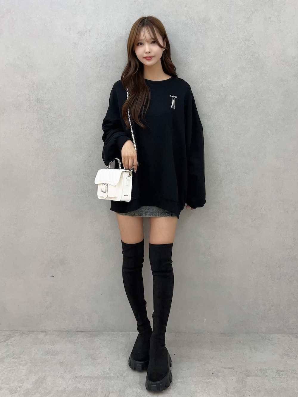 ブラック系のスウェット、ブルー系のデニムスカート、ホワイト系のショルダーバッグを着用したレディースの秋コーディネートの2枚目の写真