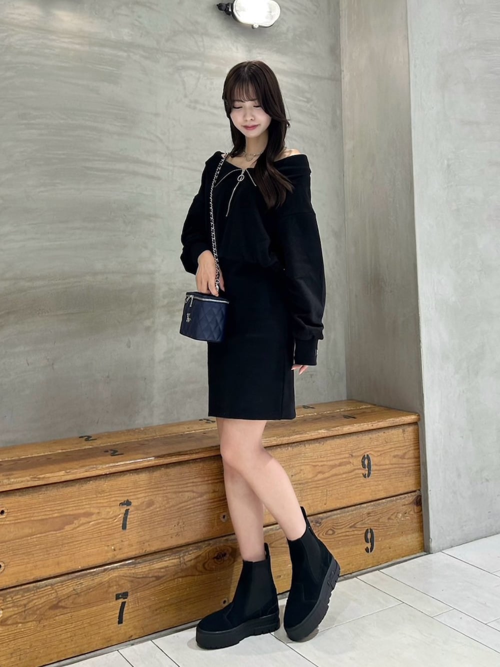 ブラック系のワンピース、ブルー系のハンドバッグ、シルバー系のネックレスを着用したレディースの秋コーディネートの2枚目の写真