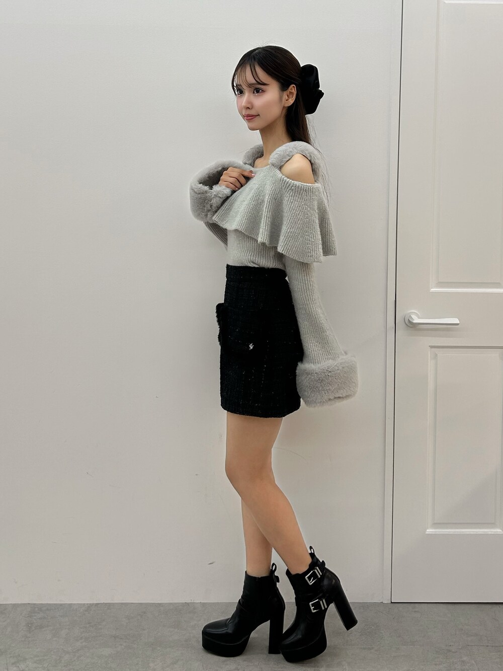 グレー系のニット/セーター、ブラック系のスカート、ブラック系のブーツを着用したレディースの秋コーディネートの2枚目の写真