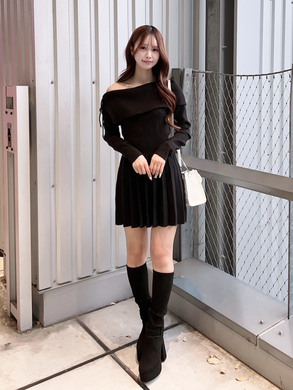 ブラック系のワンピース、ホワイト系のハンドバッグ、ブラック系のブーツを着用したレディースの冬コーディネートの2枚目の写真