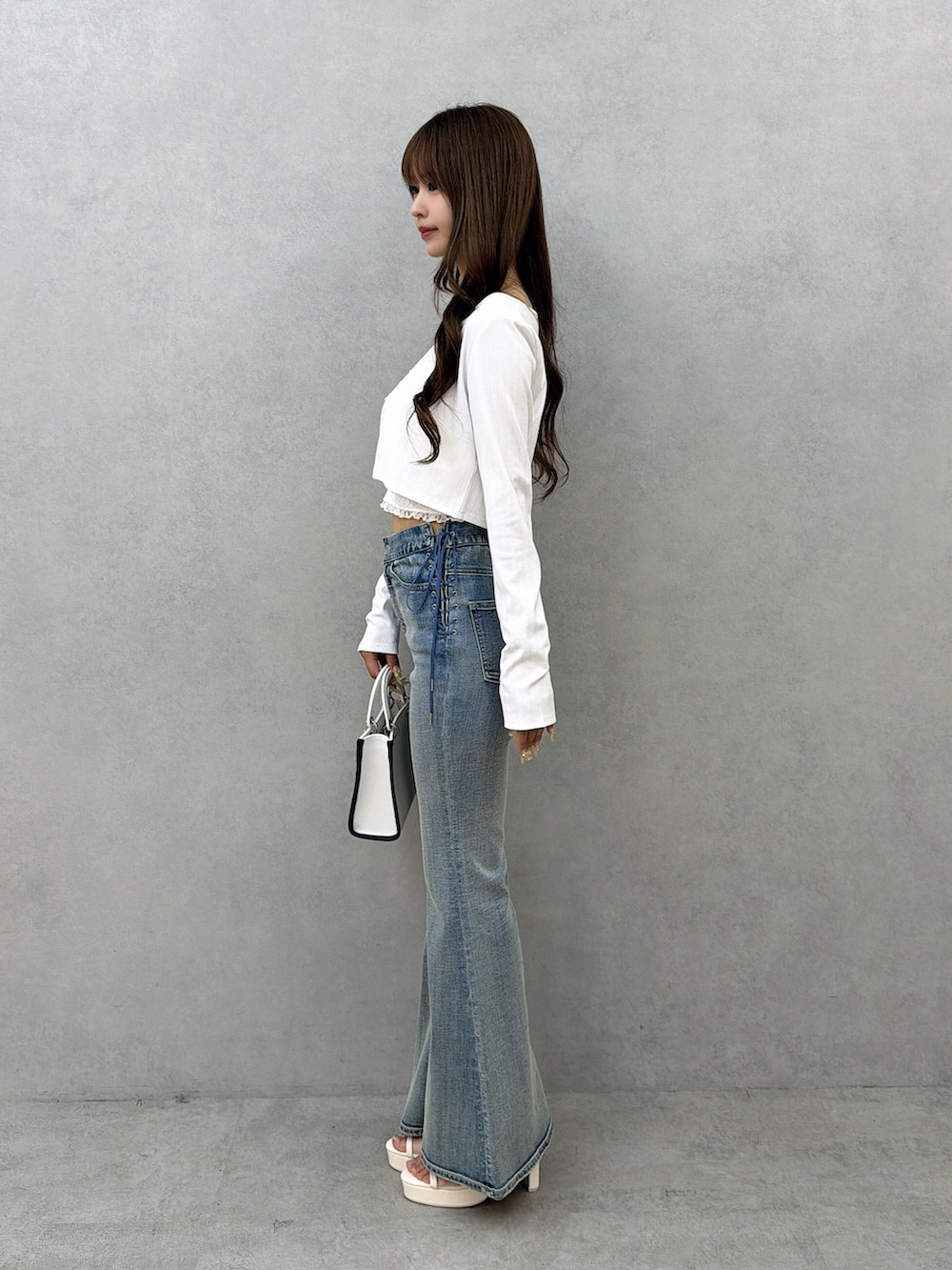 ブルー系のデニムパンツ、ホワイト系のサンダル、ホワイト系のショルダーバッグを着用したレディースの春コーディネートの3枚目の写真