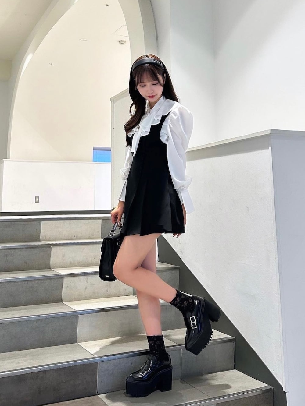 ブラック系のローファー、ホワイト系のシャツ/ブラウス、ブラック系のジャンパースカートを着用したレディースの秋コーディネートの2枚目の写真