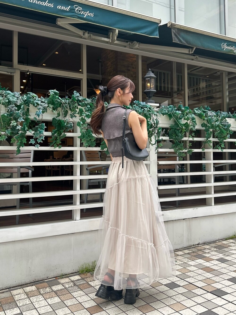 グレー系のニット/セーター、ベージュ系のスカート、ブラック系のショルダーバッグを着用したレディースの春コーディネートの2枚目の写真