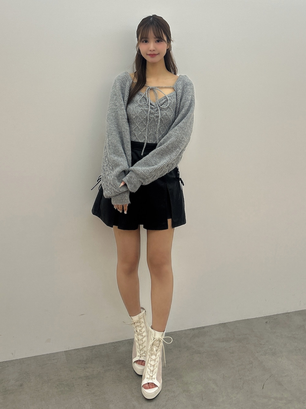 グレー系のニット/セーター、ブラック系のスカート、ホワイト系のブーツを着用したレディースの冬コーディネートの2枚目の写真