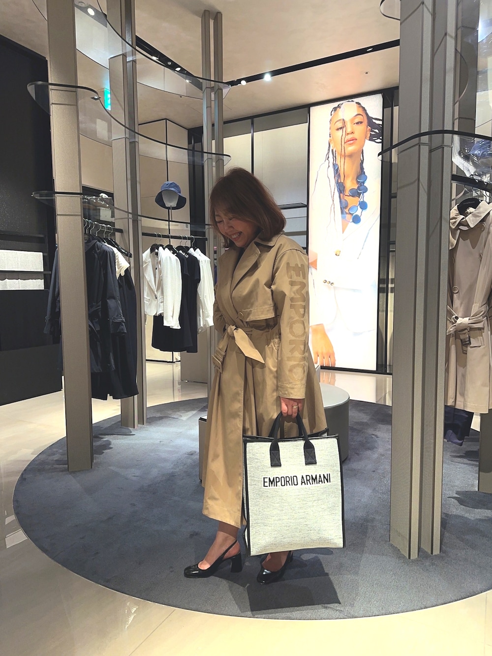 グレー系のトートバッグ、ベージュ系のトレンチコート、ブラック系のワンピースを着用したレディースの春コーディネートの2枚目の写真