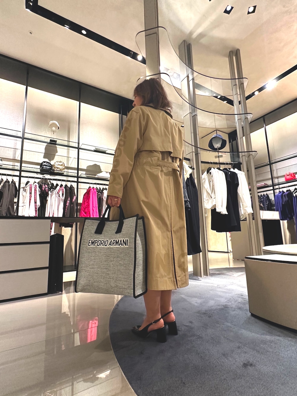 グレー系のトートバッグ、ベージュ系のトレンチコート、ブラック系のワンピースを着用したレディースの春コーディネートの3枚目の写真