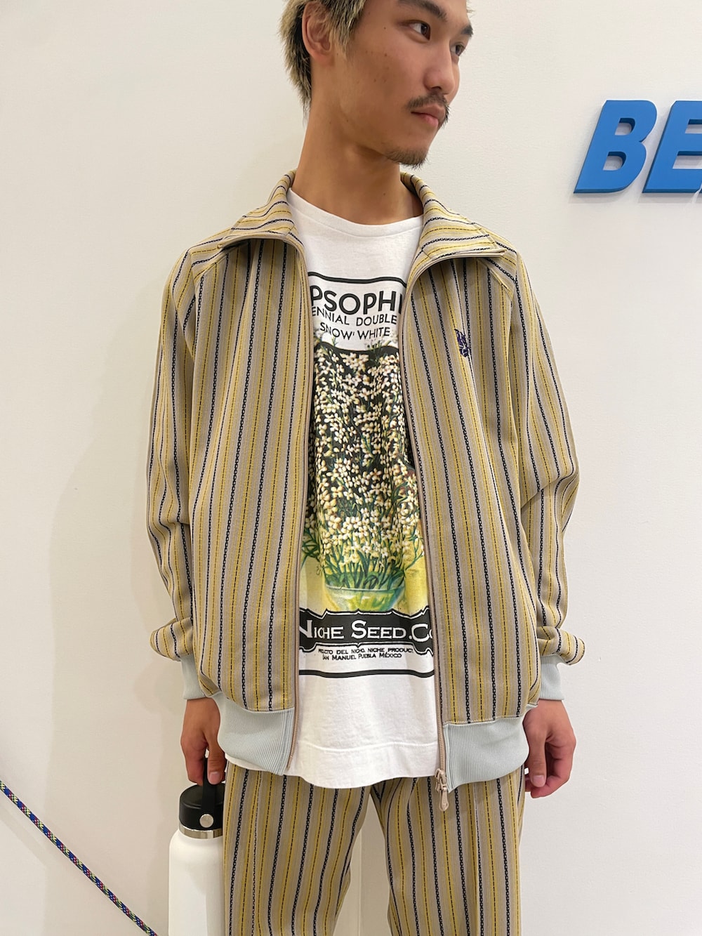 「ジャケット、坊主、休日スタイル、春、リラックススタイル、トラックジャケット、ヒゲ、ニードルス、白Tシャツ、水筒」｜「niche.のniche./ニッチ　Flower Seeds Ｔ-Shirts　フラワーシードＴシャツ（Tシャツ/カットソー、ホワイト系）」を使った、スバルさん（メンズ・165cm）の春コーディネートの2枚目の写真
