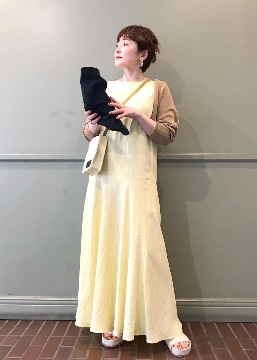ベージュ系のショルダーバッグ、ベージュ系のサンダル、イエロー系のワンピースを着用したレディースの春コーディネートの2枚目の写真