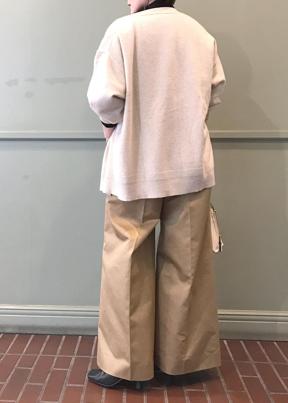 ホワイト系のハンドバッグ、ブラック系のブーツ、ベージュ系のチノパンツを着用したレディースの秋コーディネートの3枚目の写真