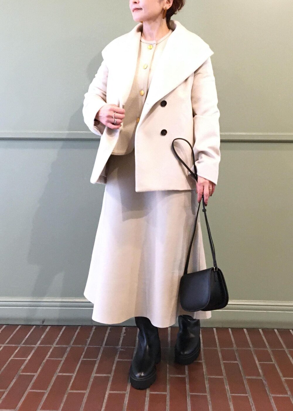ブラック系のショルダーバッグ、ホワイト系のステンカラーコート、ブラック系のブーツを着用したレディースの秋コーディネートの3枚目の写真