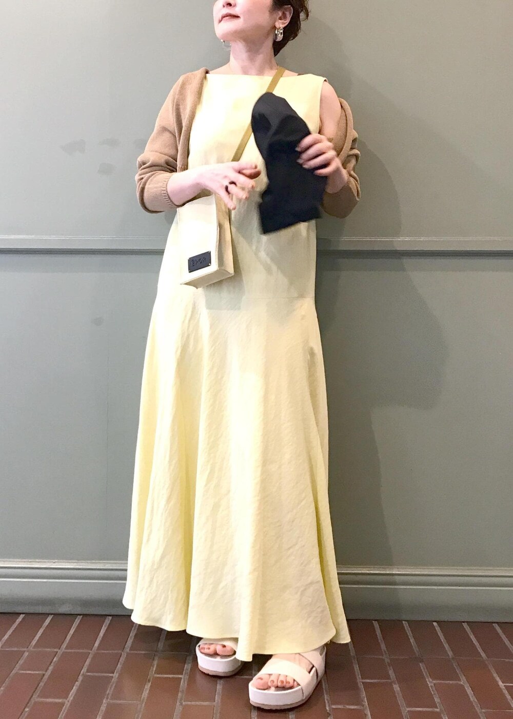 ベージュ系のショルダーバッグ、ベージュ系のサンダル、イエロー系のワンピースを着用したレディースの春コーディネートの4枚目の写真