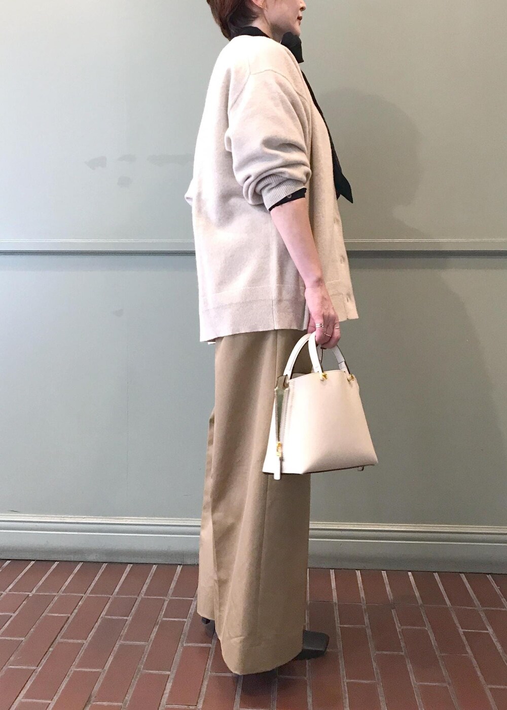 ホワイト系のハンドバッグ、ブラック系のブーツ、ベージュ系のチノパンツを着用したレディースの秋コーディネートの4枚目の写真