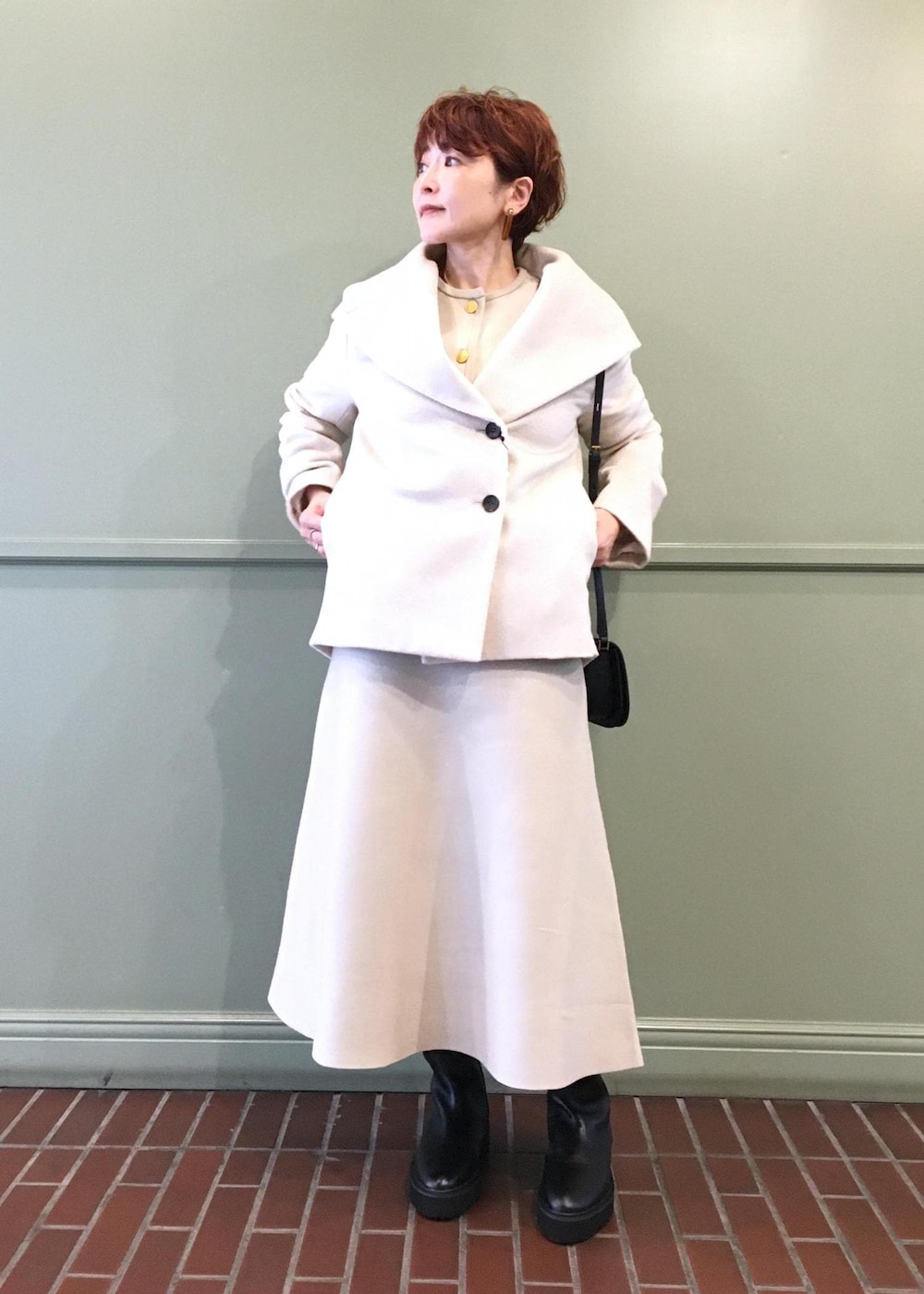 ブラック系のショルダーバッグ、ホワイト系のステンカラーコート、ブラック系のブーツを着用したレディースの秋コーディネートの5枚目の写真