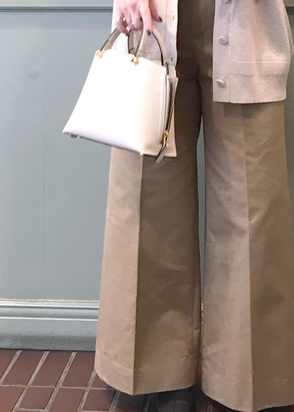 ホワイト系のハンドバッグ、ブラック系のブーツ、ベージュ系のチノパンツを着用したレディースの秋コーディネートの5枚目の写真