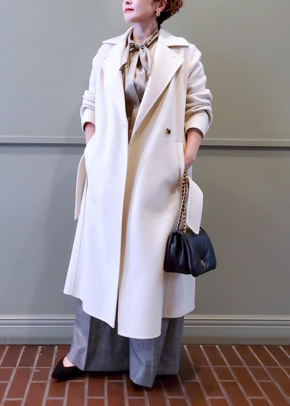 ブラック系のハンドバッグ、ホワイト系のチェスターコート、ベージュ系のシャツ/ブラウスを着用したレディースの秋コーディネートの4枚目の写真